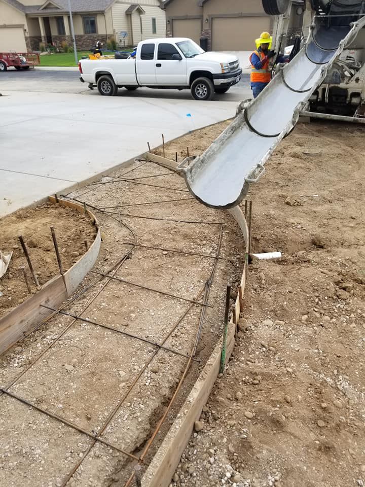 Cement truck pouring concrete into a walkway frame with rebar. Construction worker nearby.