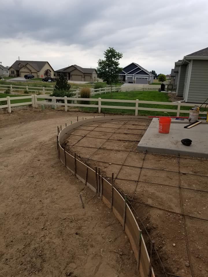 A construction site with wood forms for concrete paving, rebar grid, and patio area with a bucket.