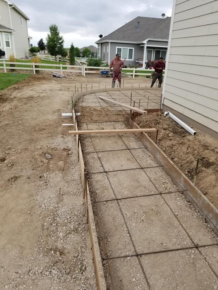 Construction of a concrete walkway with rebar in a backyard, two workers visible, residential setting.