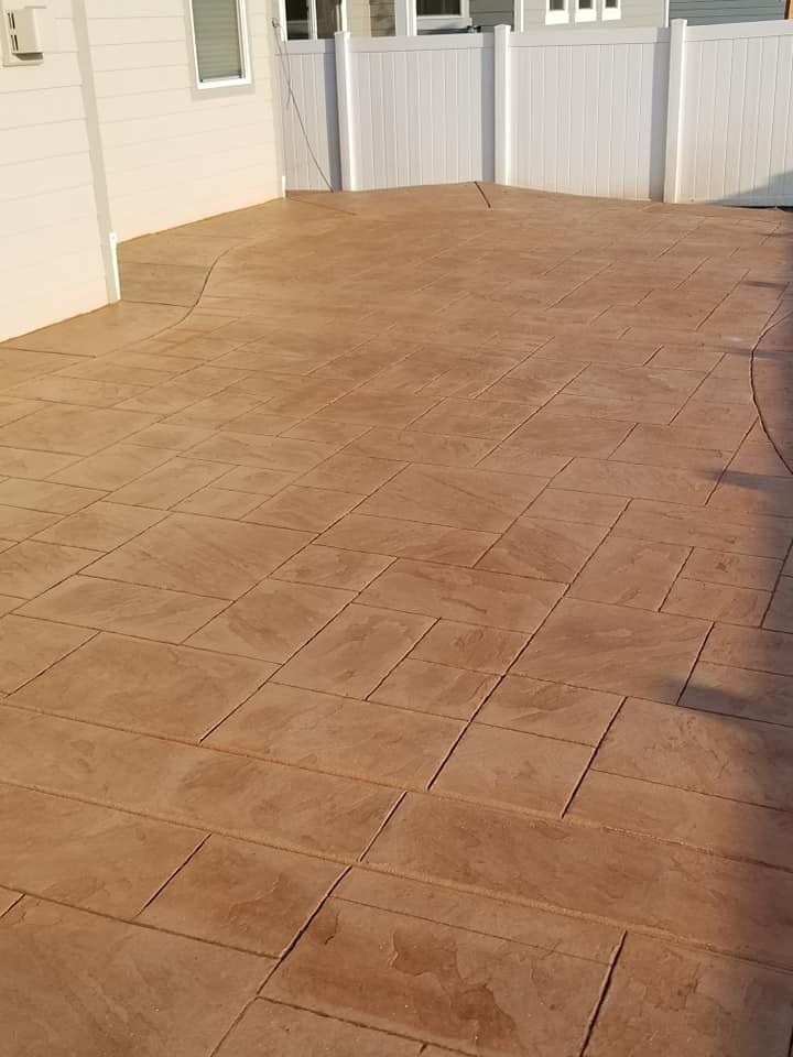 Stamped concrete patio, brown, with rectangular pattern, bordered by white fence and house.