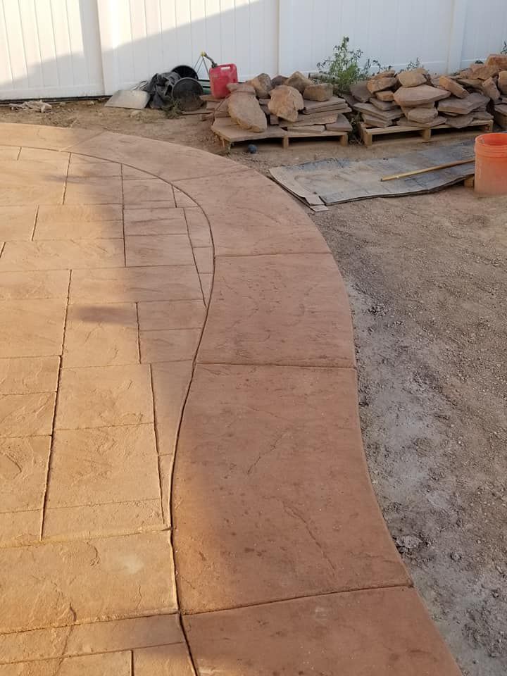 Curved brick-like concrete pathway under construction, brown-orange hue.  Materials and equipment in background.