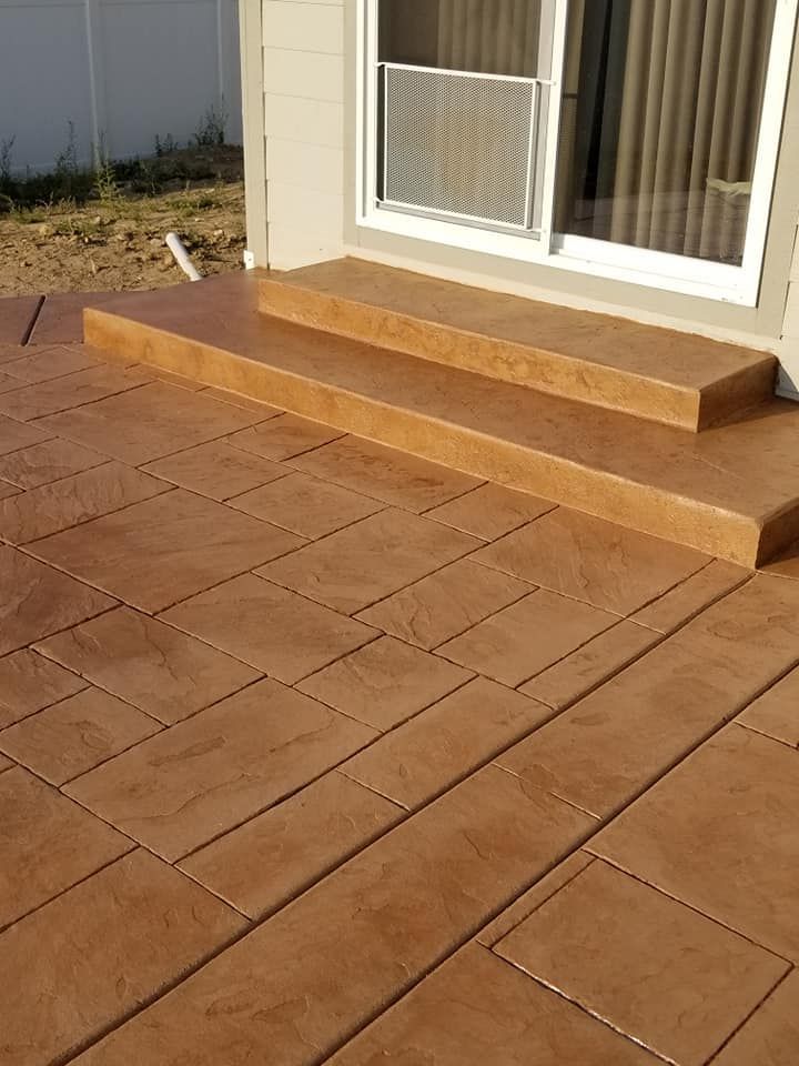 Brown stamped concrete patio with steps leading to a sliding glass door.