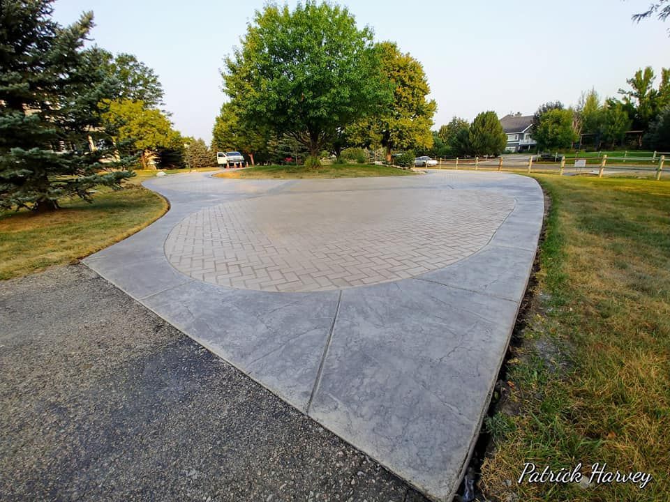 Curved concrete plaza in a park with trees, grass, and a gravel path under a clear sky