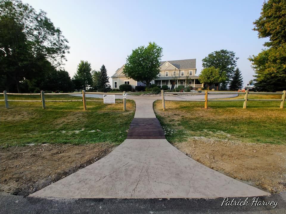 A wide path leads to a large house with a wraparound porch, flanked by wooden fences and greenery.