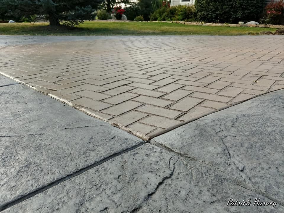 Herringbone-patterned concrete driveway, bordered by textured concrete, outdoors.