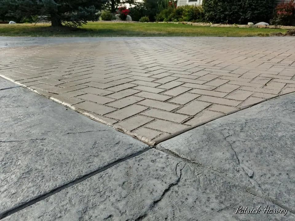 Concrete driveway with a patterned brick design, next to a plain concrete surface.