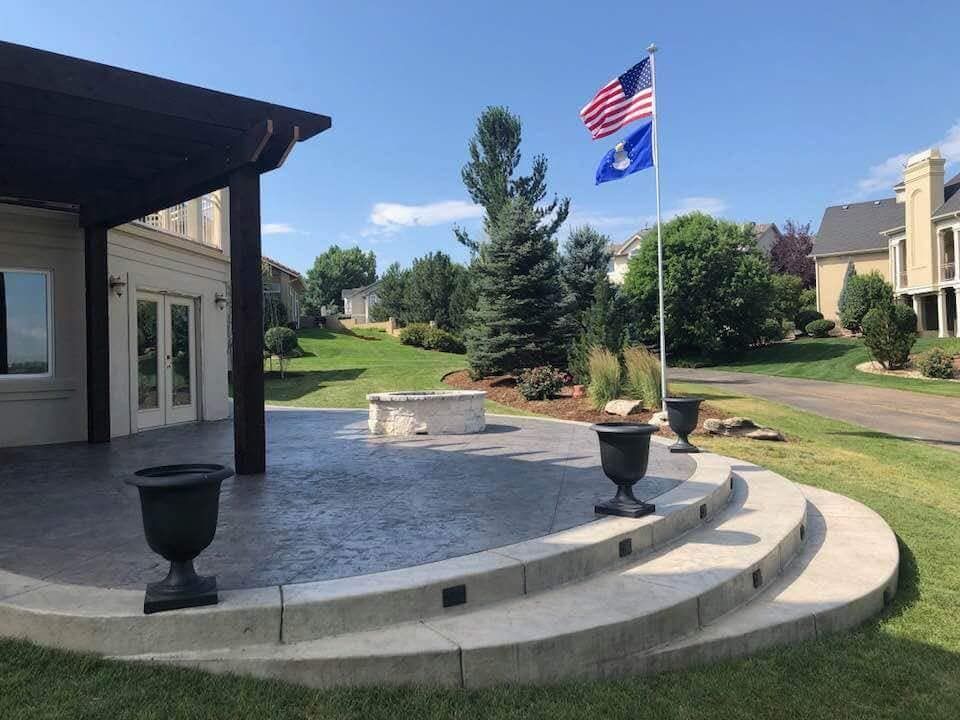 Backyard patio with flag, steps, and urns, next to a lawn, and a house.
