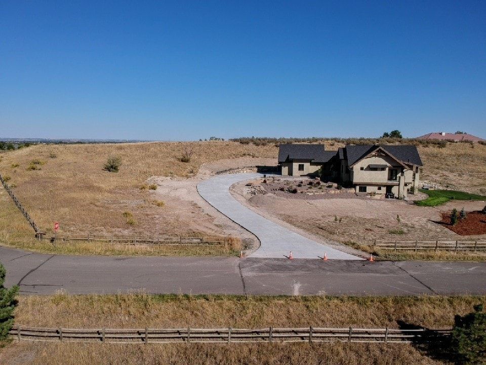 A house under construction on a grassy hill with a concrete driveway and a clear blue sky.