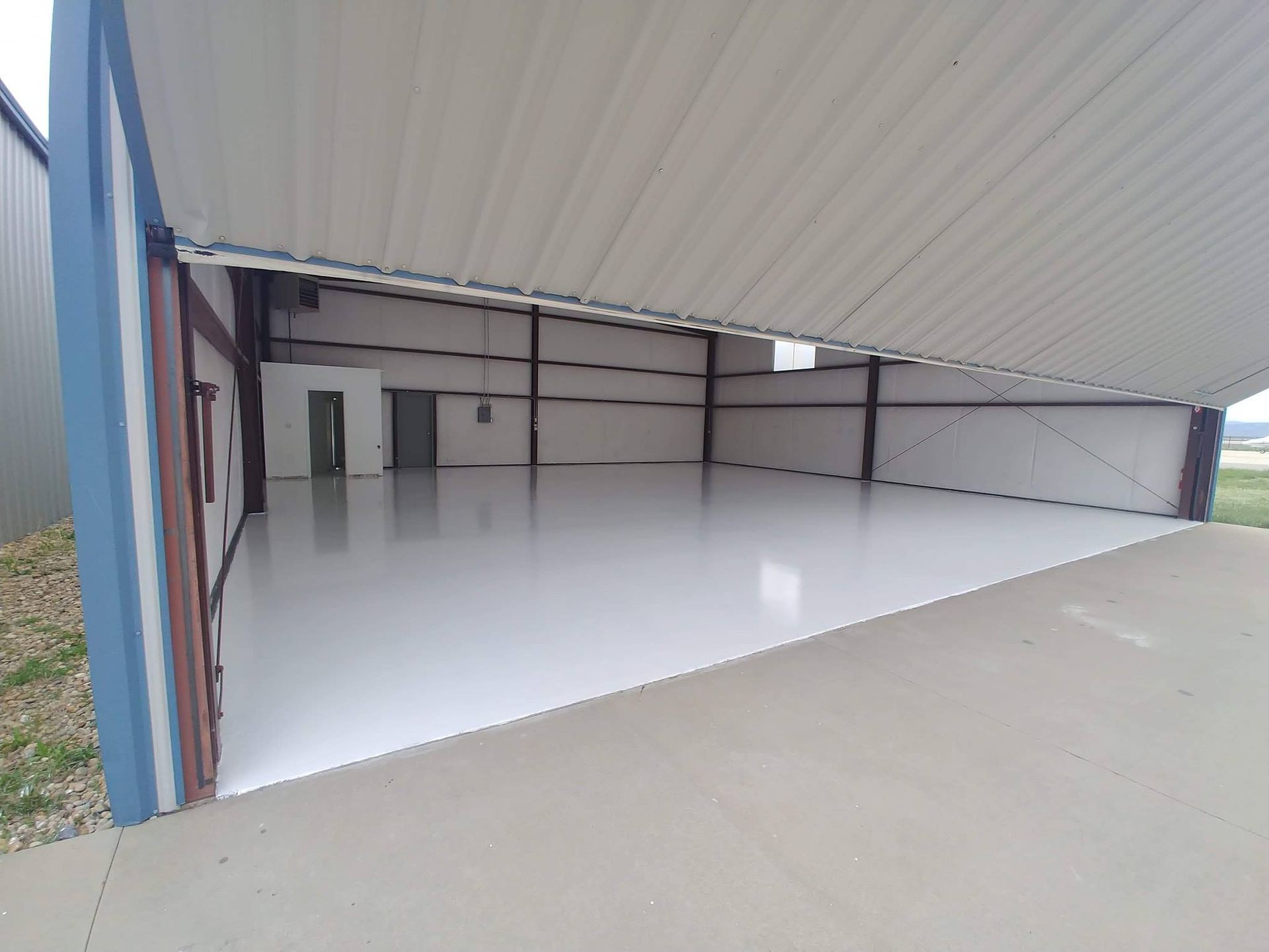 Open airplane hangar with white floor, steel beams, and a small room in the back.