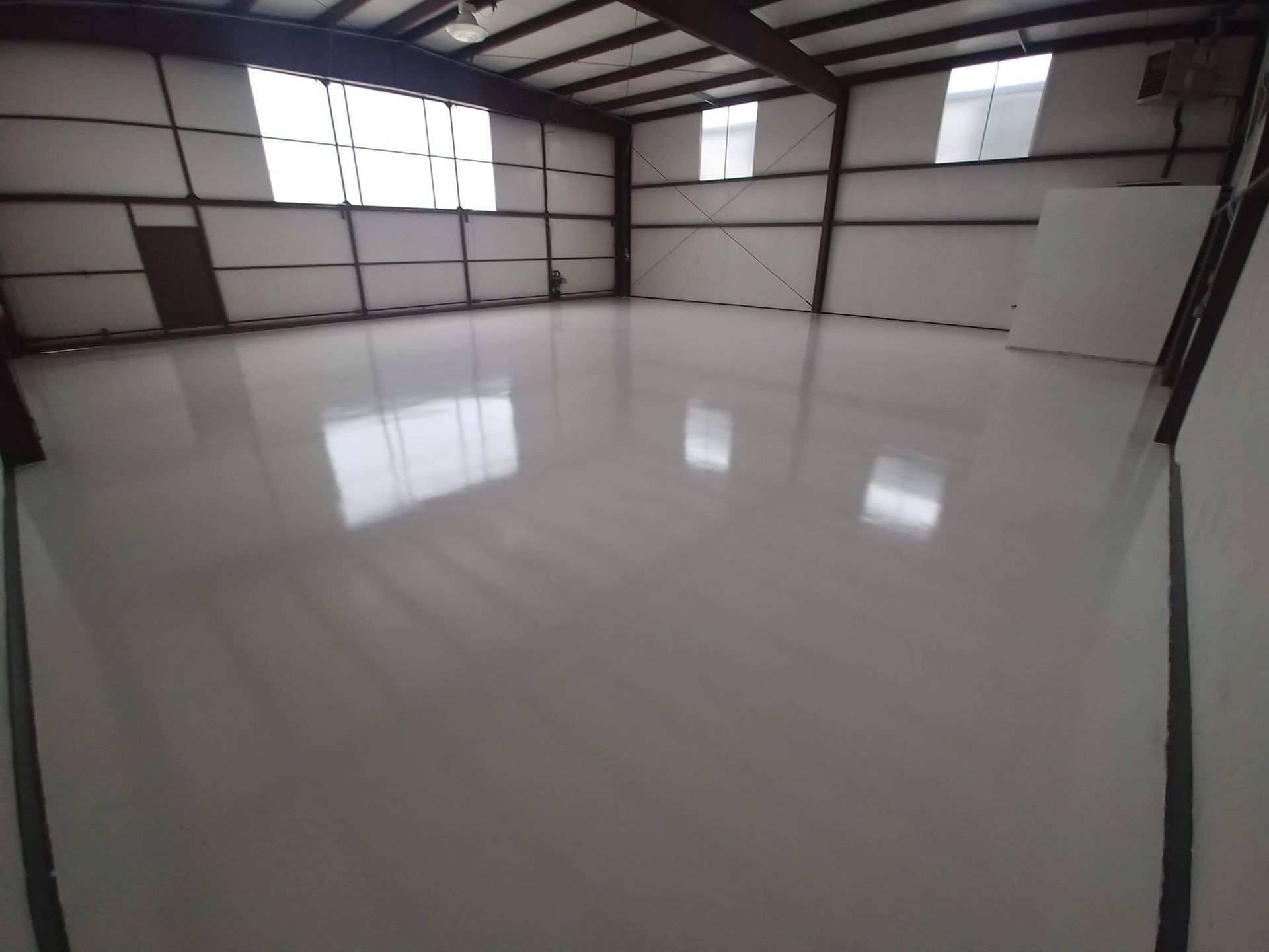Empty warehouse interior with a shiny, white floor and metal beams.