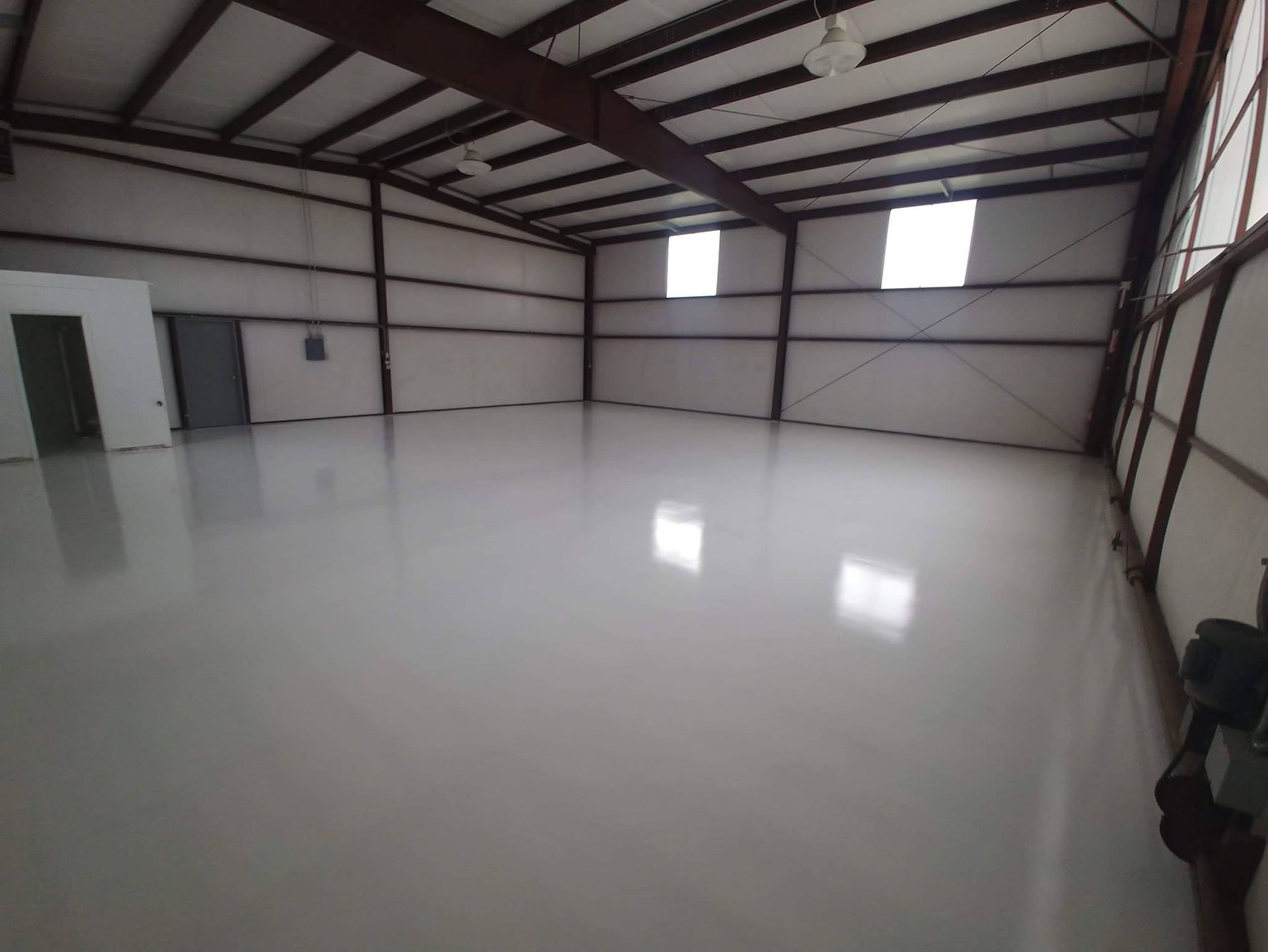 Empty, bright white warehouse interior with shiny floor and small windows.