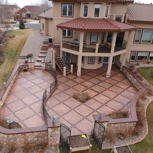 Large house with patio and steps; brown stamped concrete; balcony; green yard; cloudy sky.