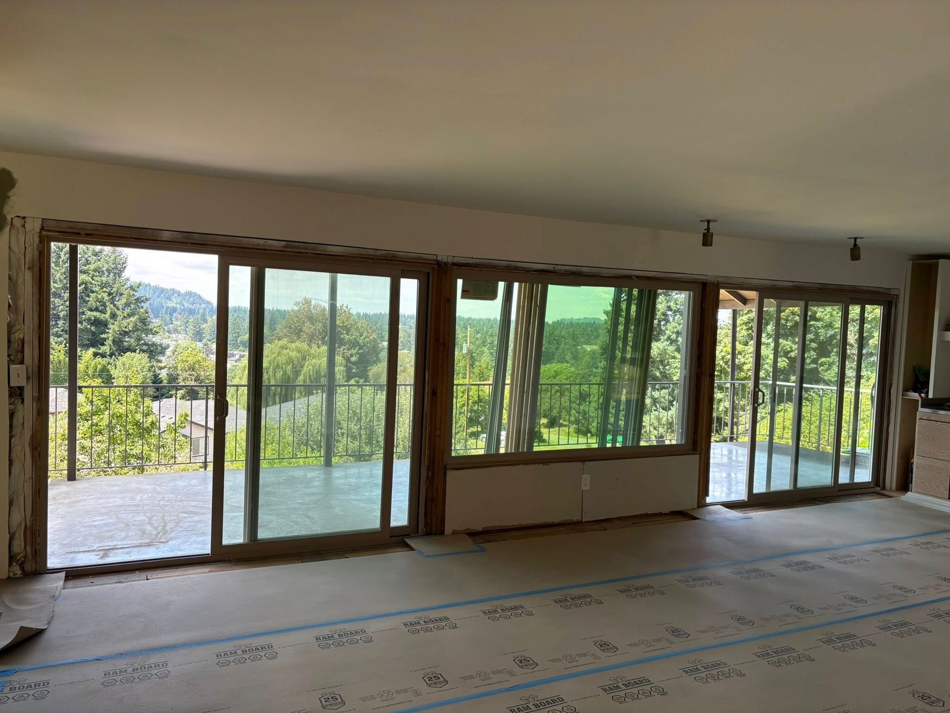 Interior view of a room with large sliding glass doors, unfinished walls, and a view of trees and a railing outside.