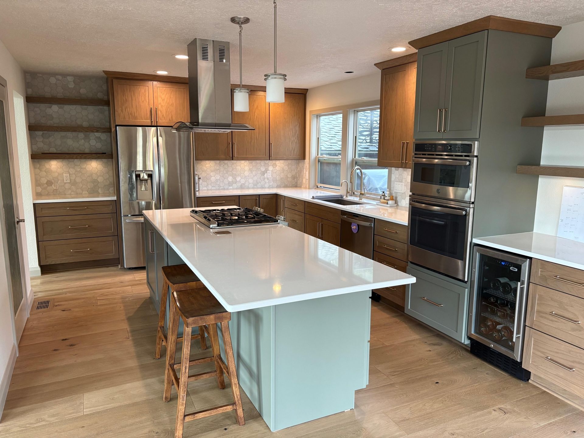 Modern kitchen with light wood cabinets, gray island, stainless steel appliances, and white countertops.