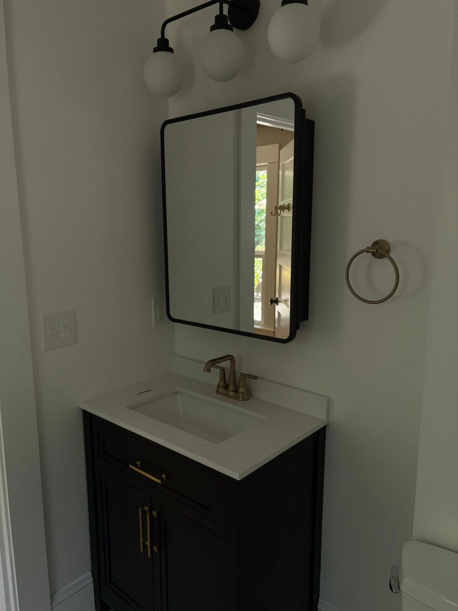 Bathroom vanity with black cabinet, white countertop, rectangular mirror, and globe light fixture.