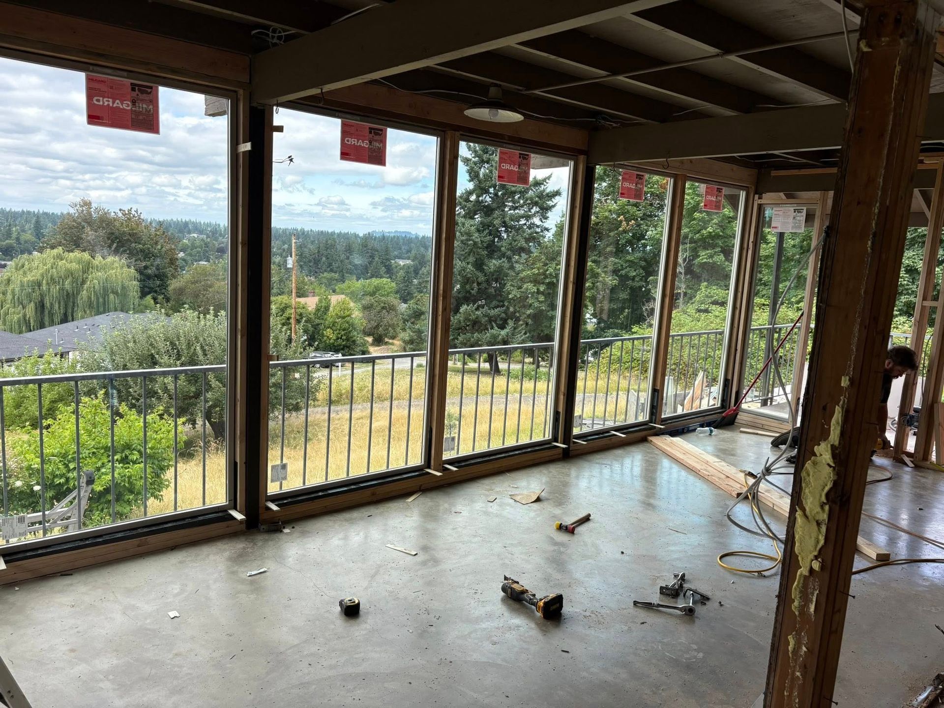 Interior view of a room under construction with large windows overlooking a green landscape. Concrete floor.