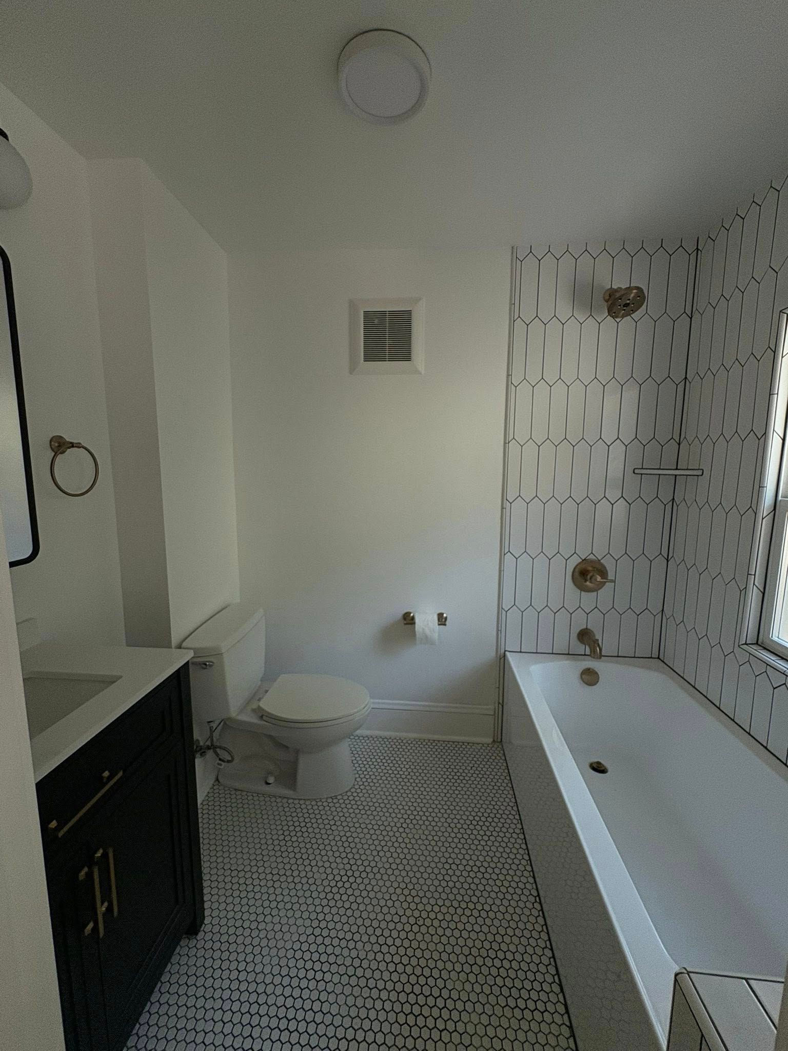 Modern bathroom with patterned floor and wall tiles, bathtub, toilet, and black vanity.