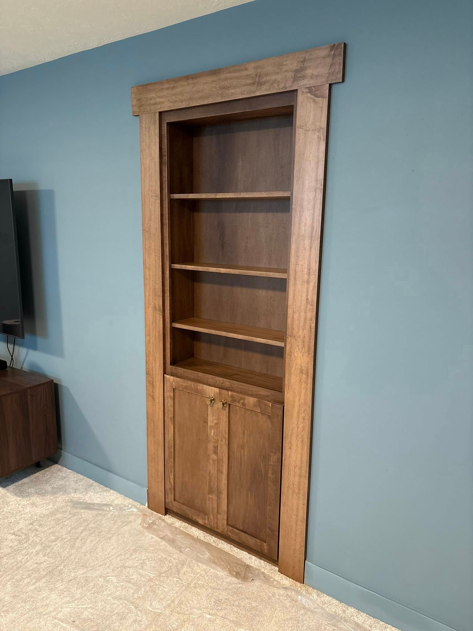 Wooden bookshelf door with shelves and cabinets, built into a blue wall.
