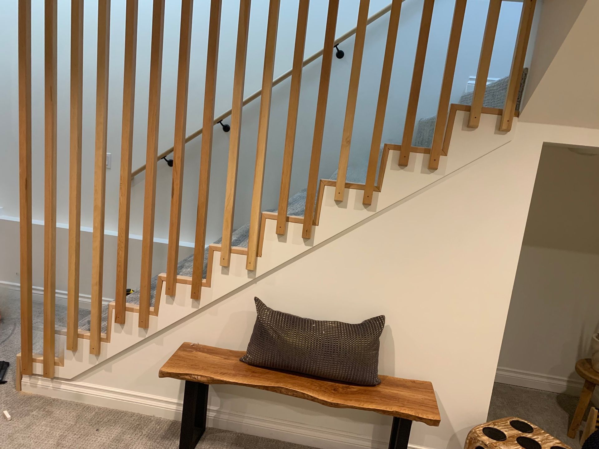 Wooden stair railing with vertical slats, above a bench with a pillow, in a well-lit interior.