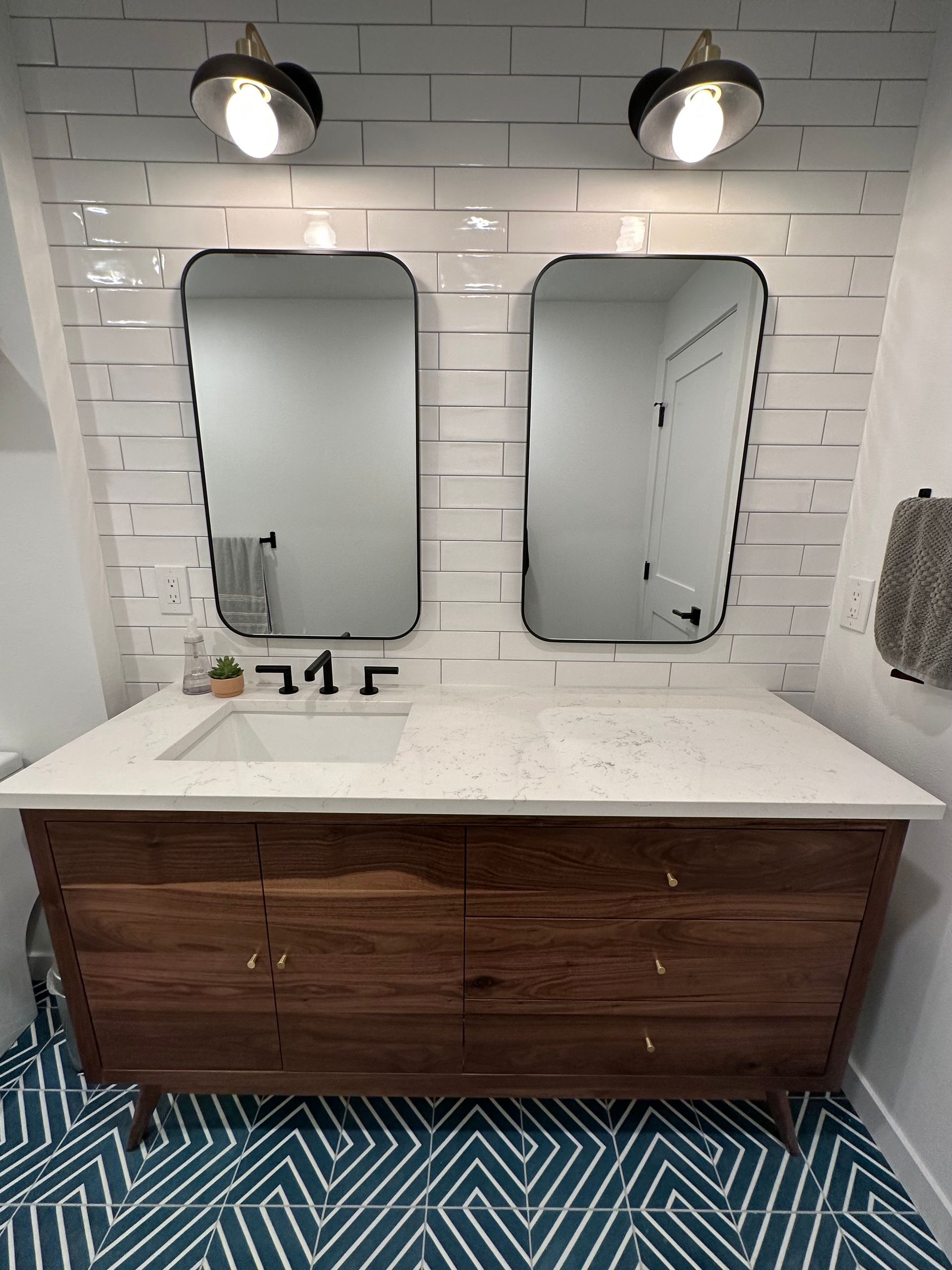Bathroom with two mirrors, wood vanity, white countertop, and patterned blue and white floor tiles.