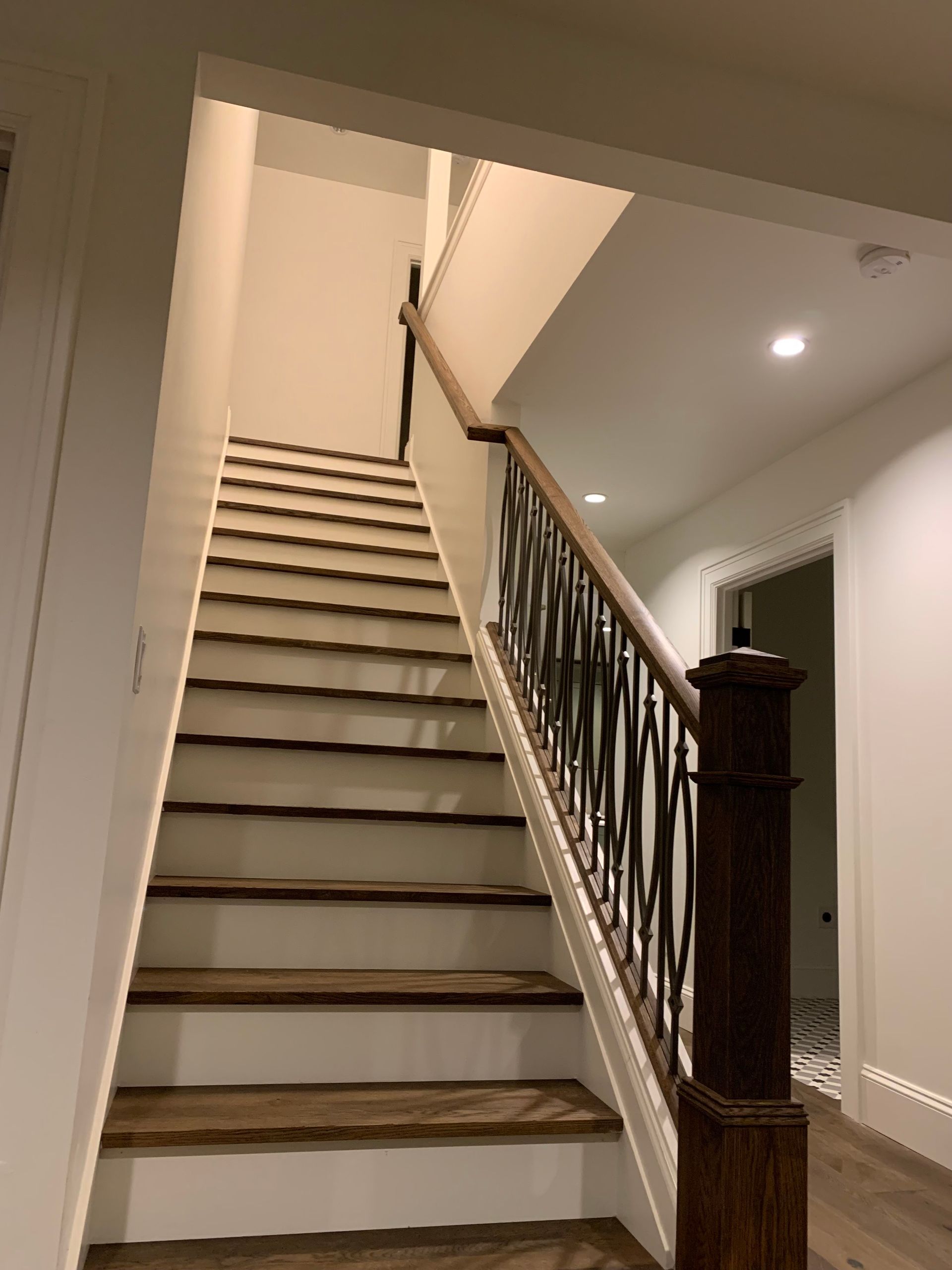 Wooden staircase with dark brown treads and white risers, leading upwards with dark railing.