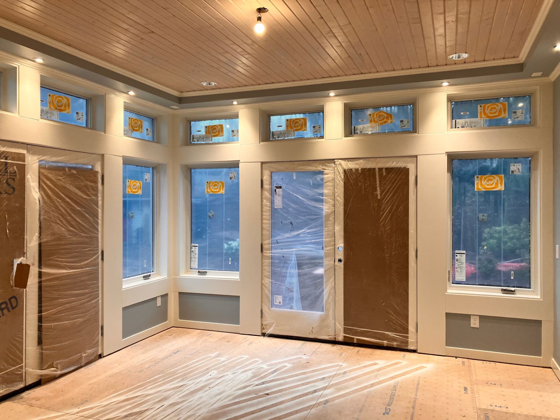 Interior of a room under construction with windows and doors covered in plastic. Wooden floor and ceiling.