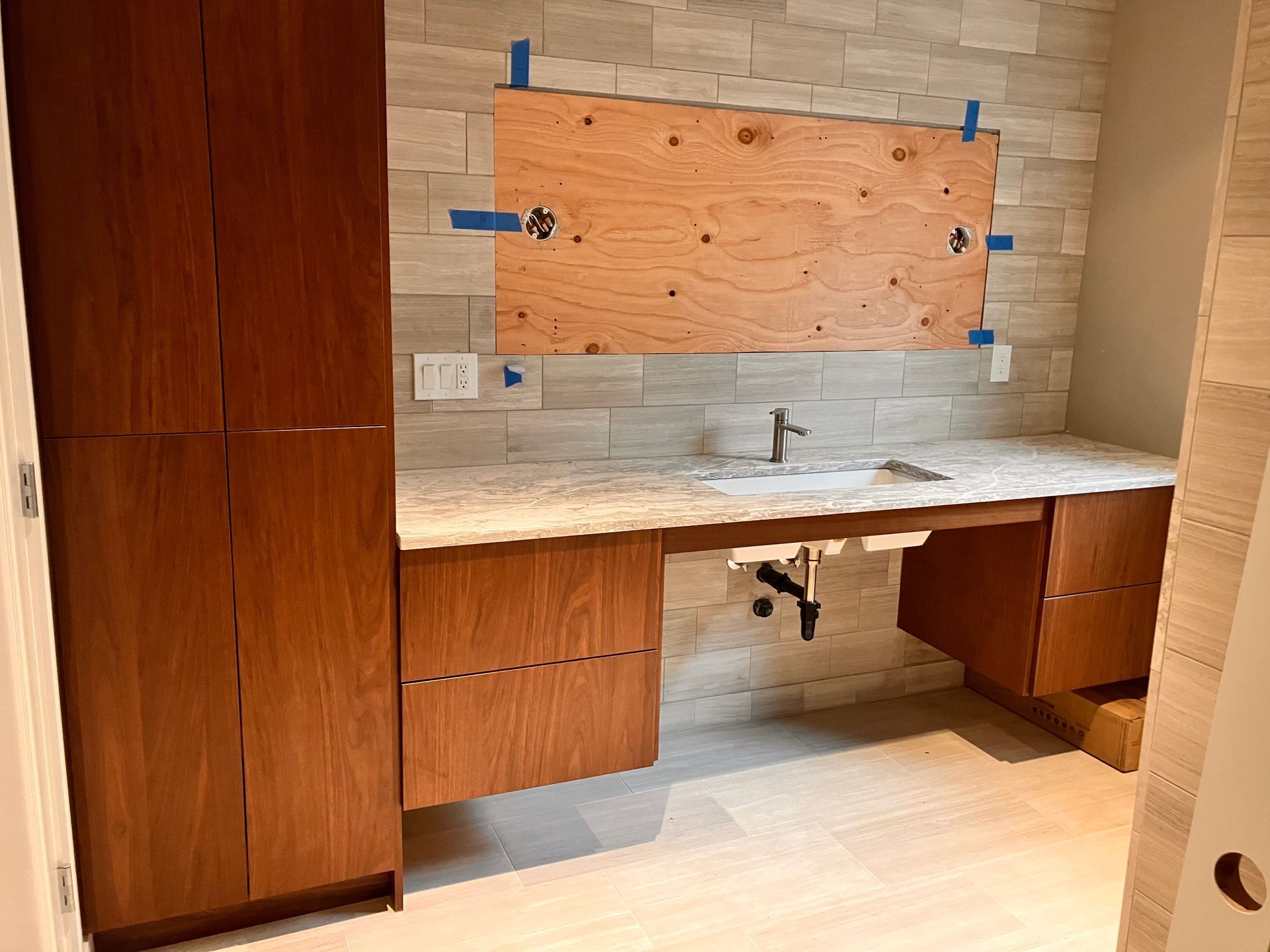 Bathroom with wood cabinets, countertop, sink, and tiled walls, still under construction.