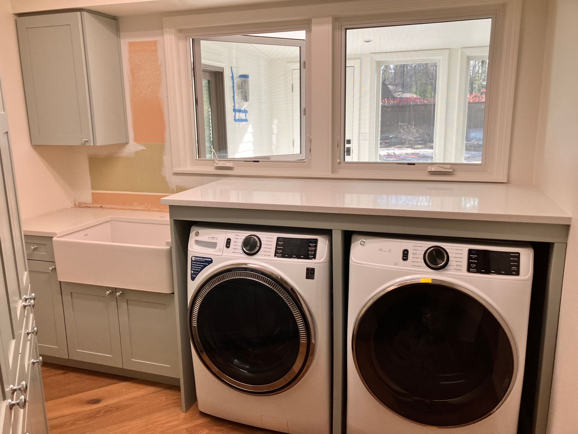 Laundry room with light blue cabinets, white appliances, and a window.