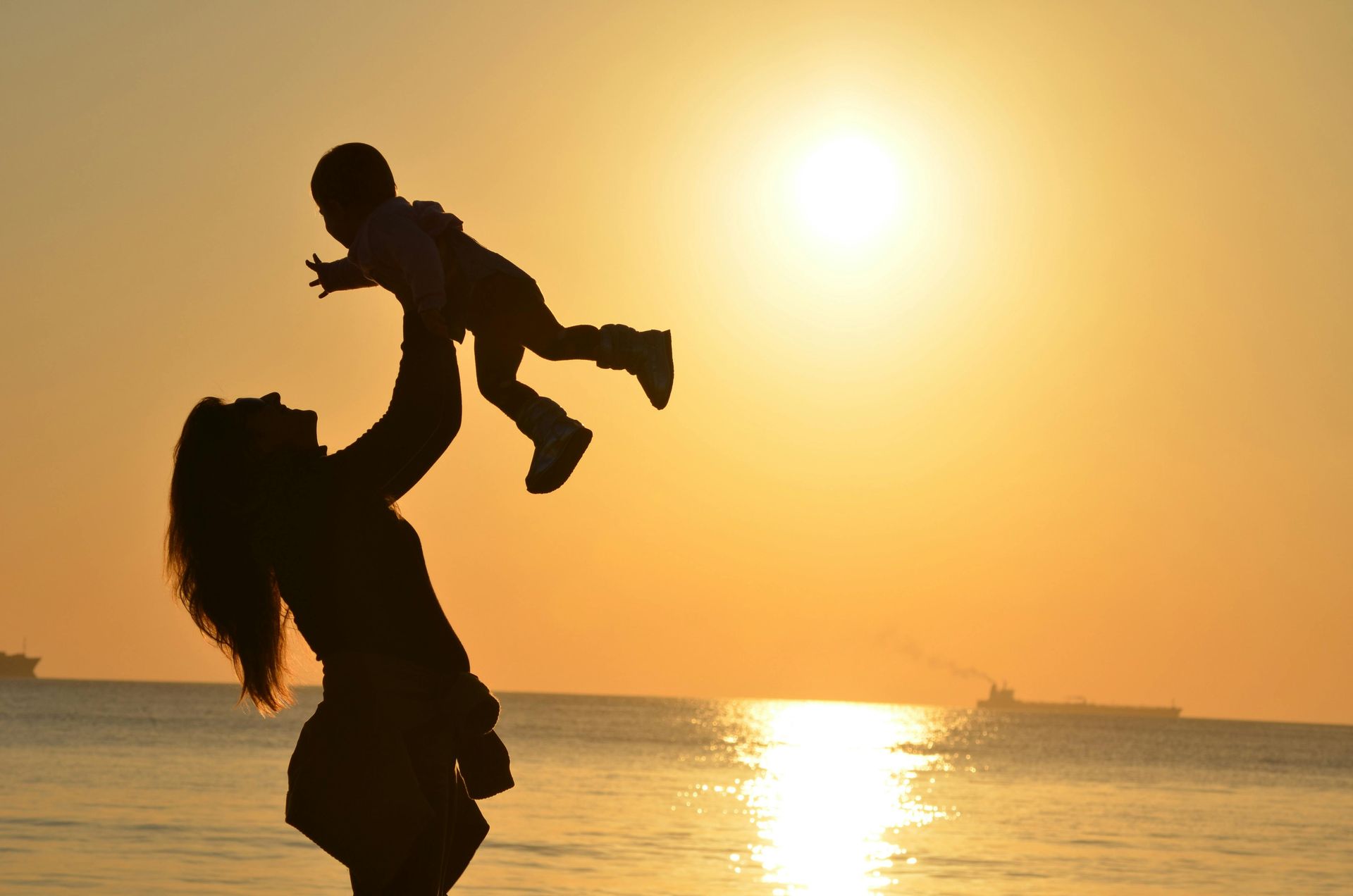 une femme tient un bébé dans ses bras avec un coucher de soleil en fond. 
Massage bébé, massage femme enceinte, maman et bébé. Colmar, Ribeauvillé, Wintzenheim, Horbourg Wihr