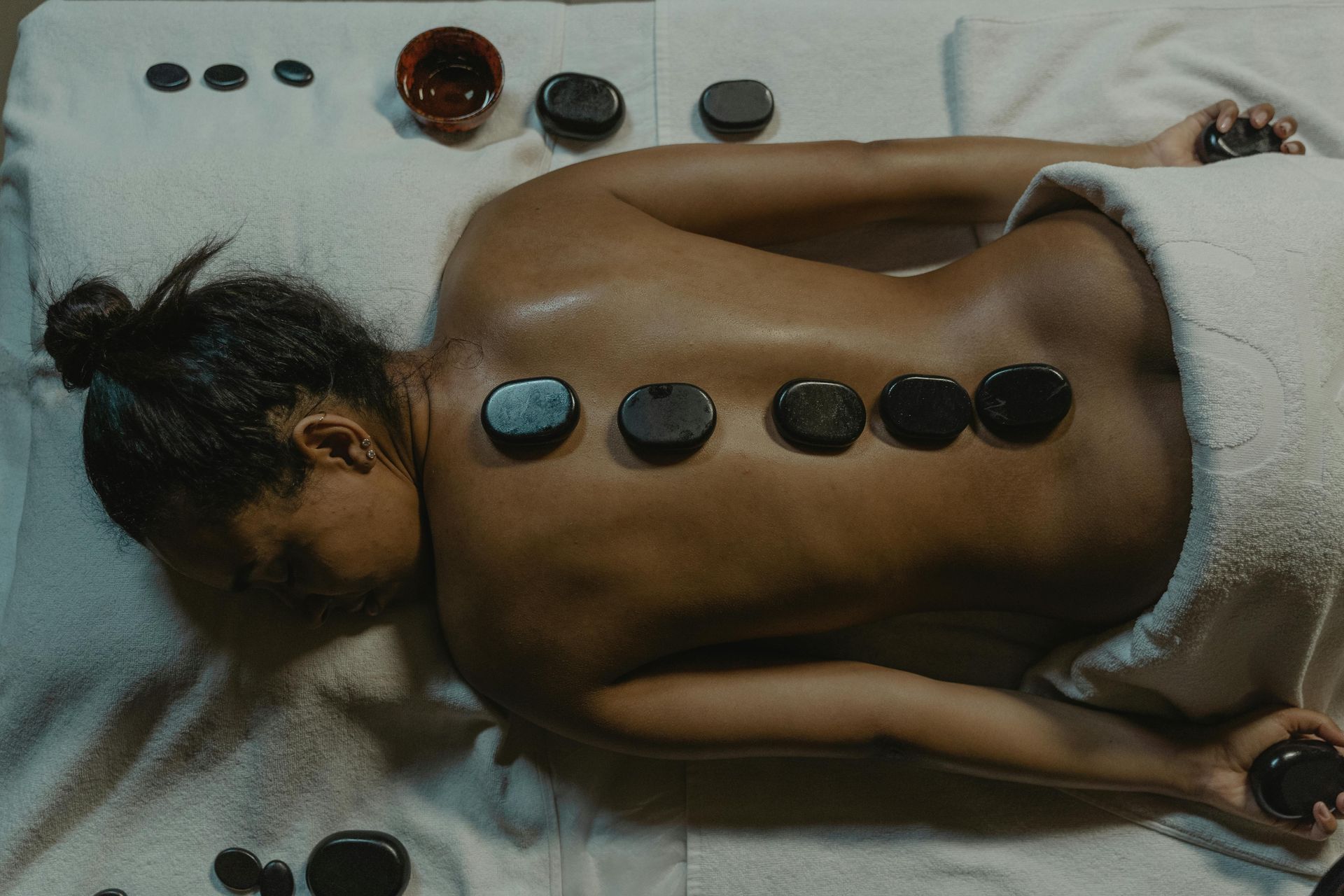 Une femme est allongée sur un lit et reçoit un massage avec des pierres sur le dos.