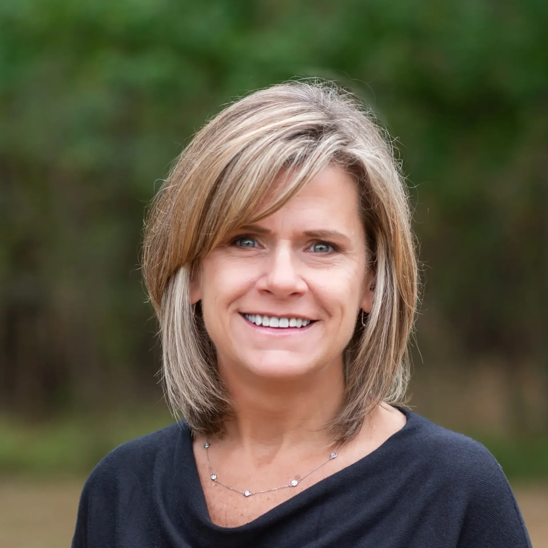 A woman wearing a black shirt and a necklace smiles for the camera