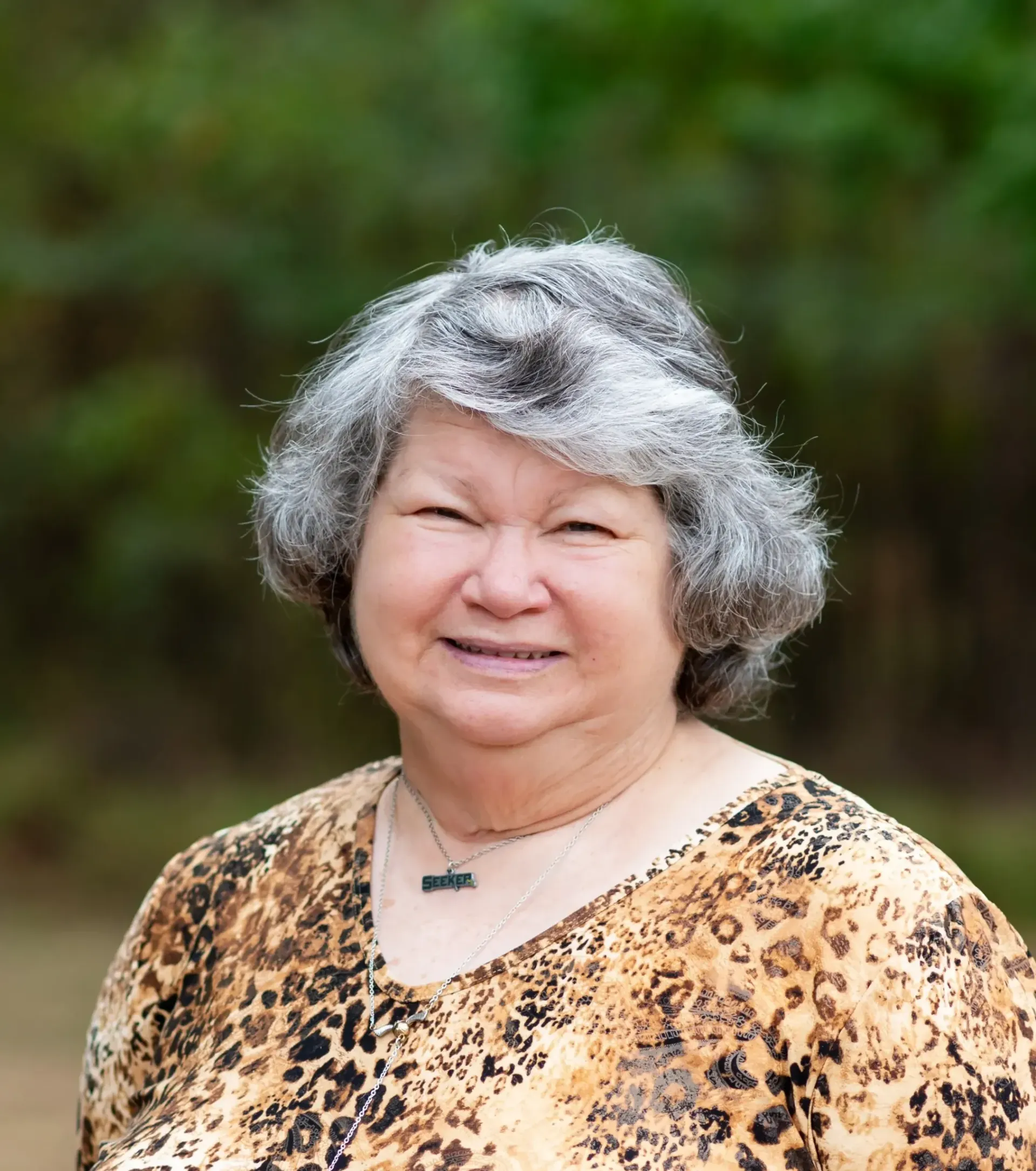 A woman with gray hair and a leopard print shirt is smiling for the camera.