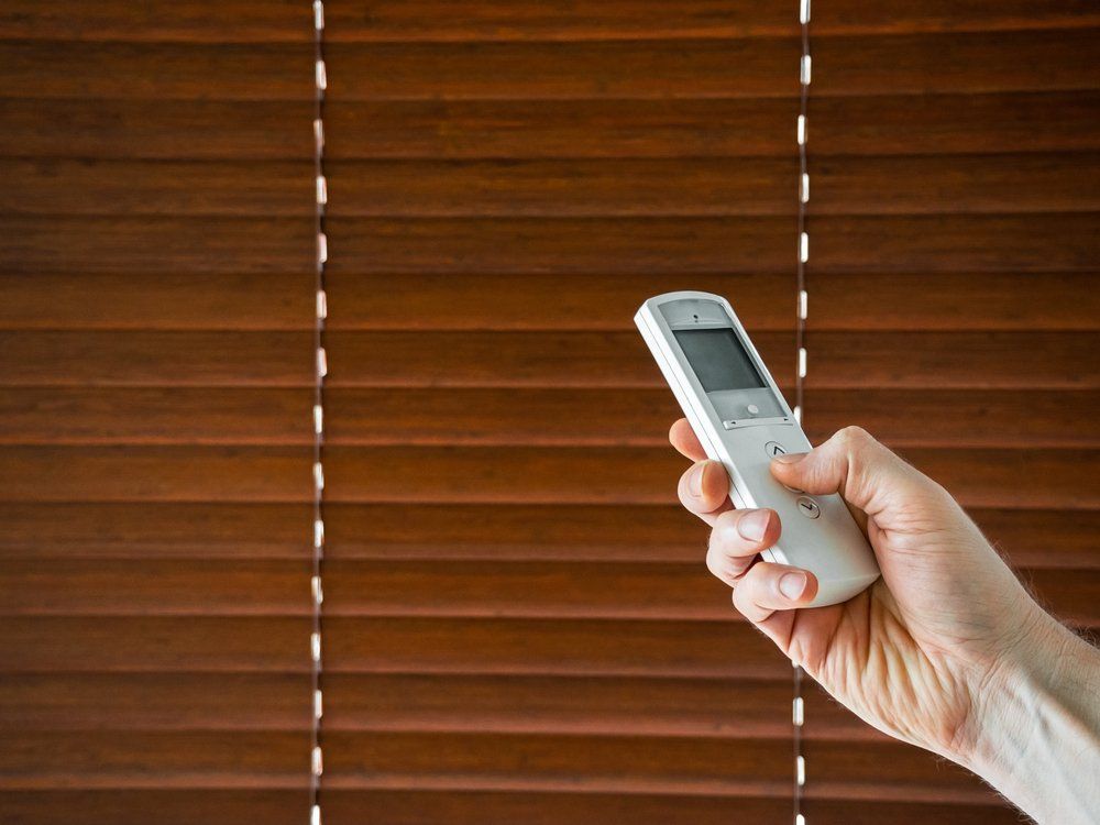 Man Holds A Remote Control To Open The Window Blinds — Studio Curtains & Blinds in Mount Gravatt, QLD