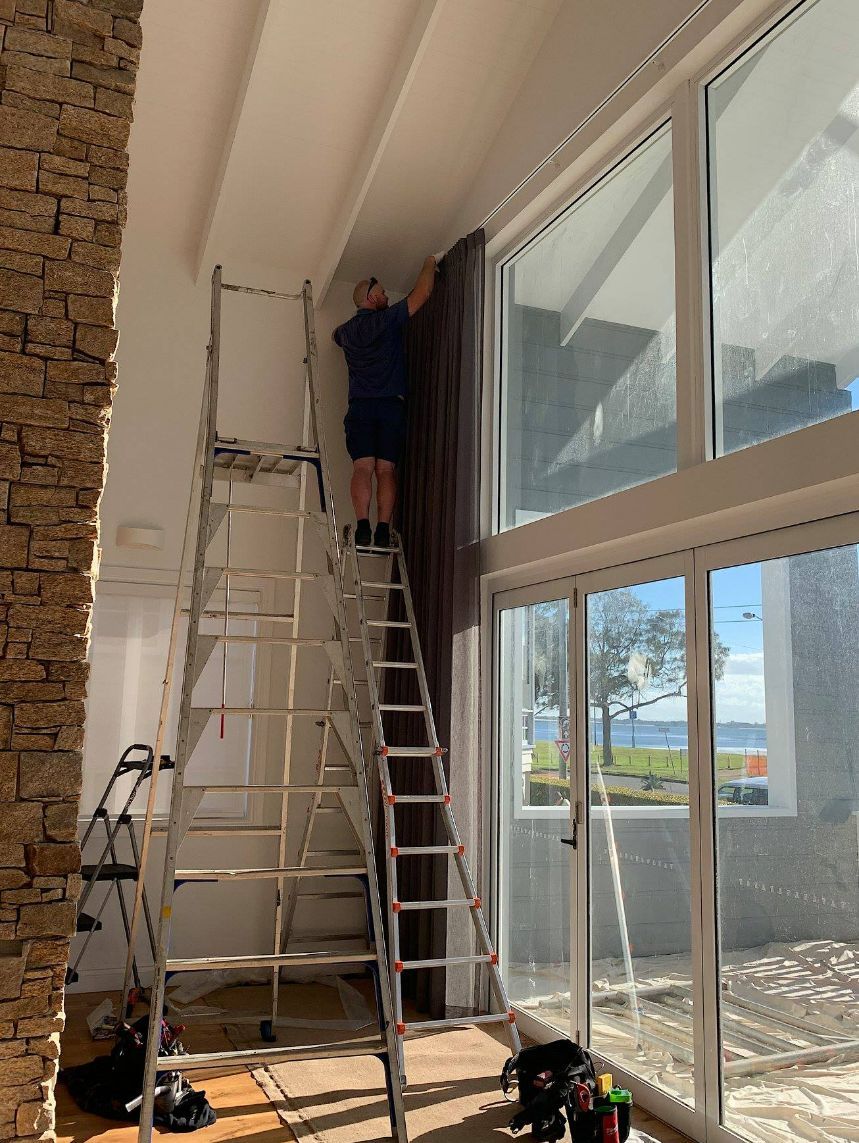 Man On A Ladder Installing Motorised Curtains — Electric Curtains in Brisbane, QLD