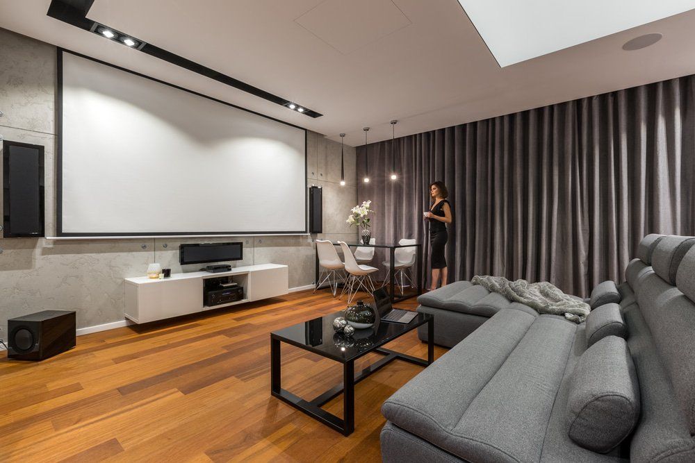 Woman In A Living Room & A Grey Curtains Behind Her — Studio Curtains & Blinds in Mount Gravatt, QLD