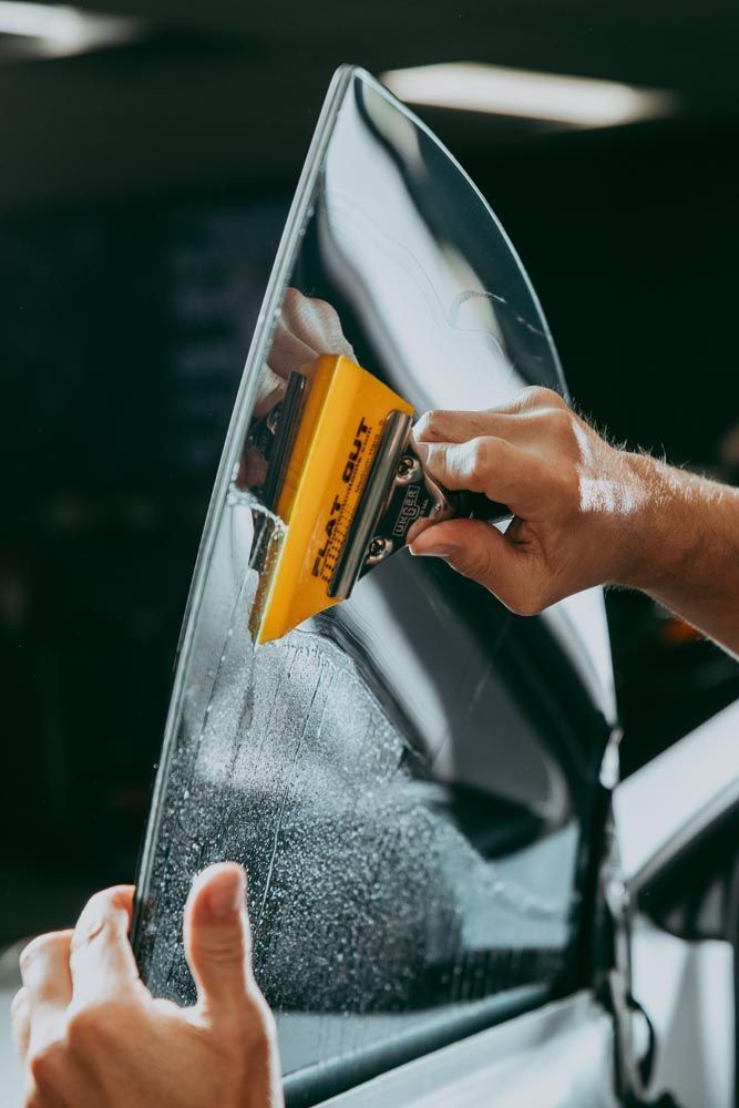 A person applying tinted film to a car window using a yellow squeegee.