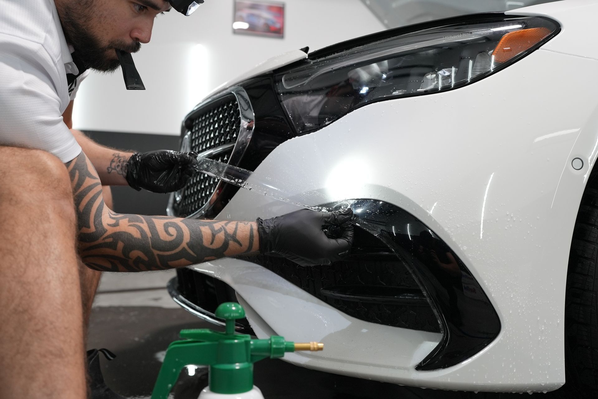 A man is cleaning the front bumper of a white car.