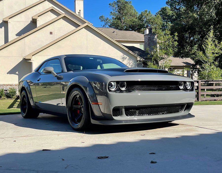 a gray dodge challenger is parked in a driveway in front of a house .