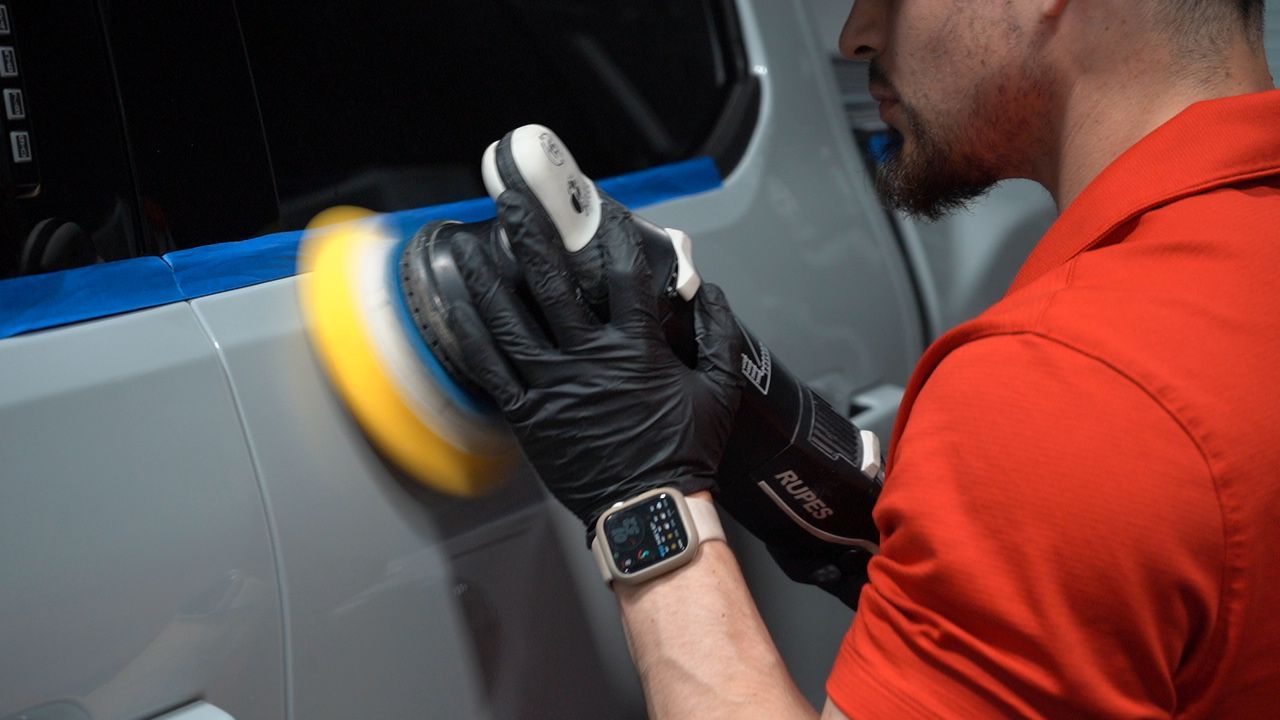 a person is polishing a car in front of a red van
