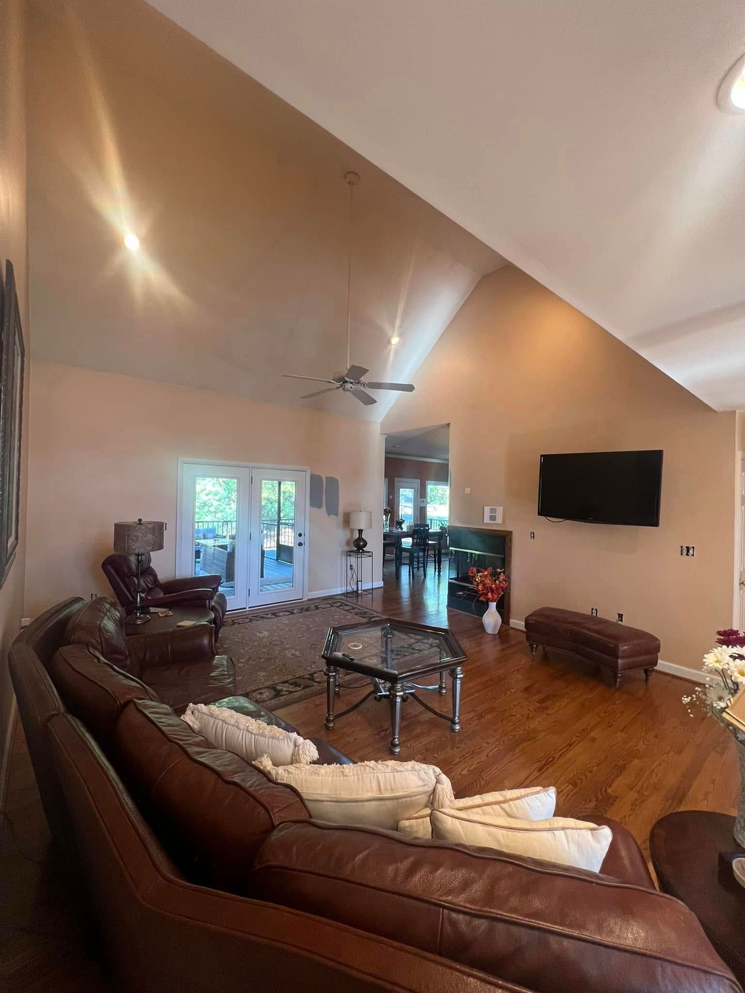 Spacious living room with leather sofa, TV, vaulted ceiling, French doors, and wood floors.