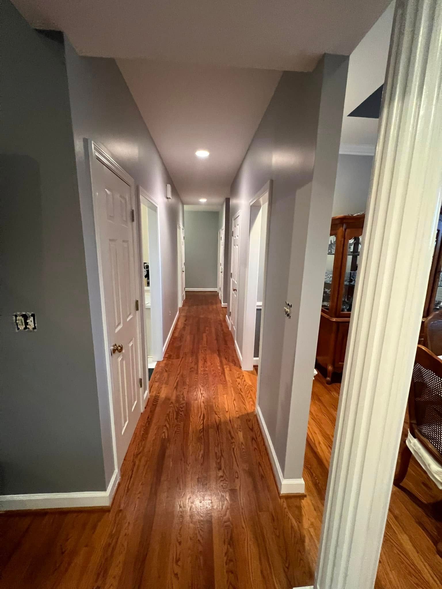 Long hallway with hardwood floors, gray walls, and white doors.