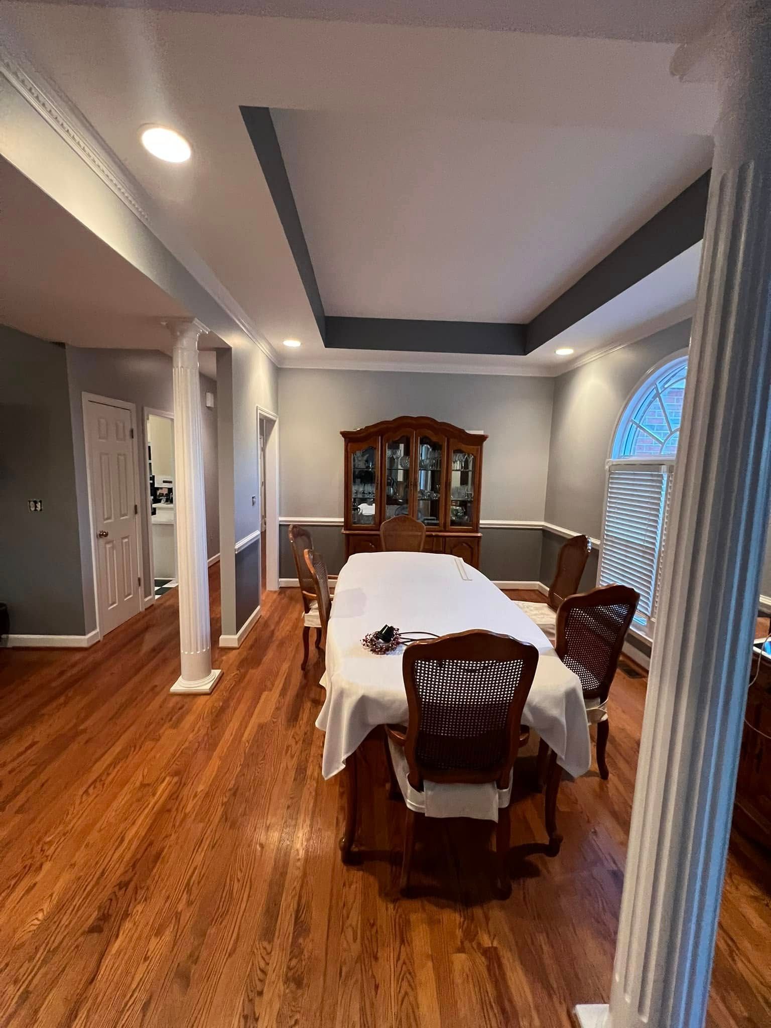 Formal dining room with wood floor, large table set with white cloth, and a wooden hutch.