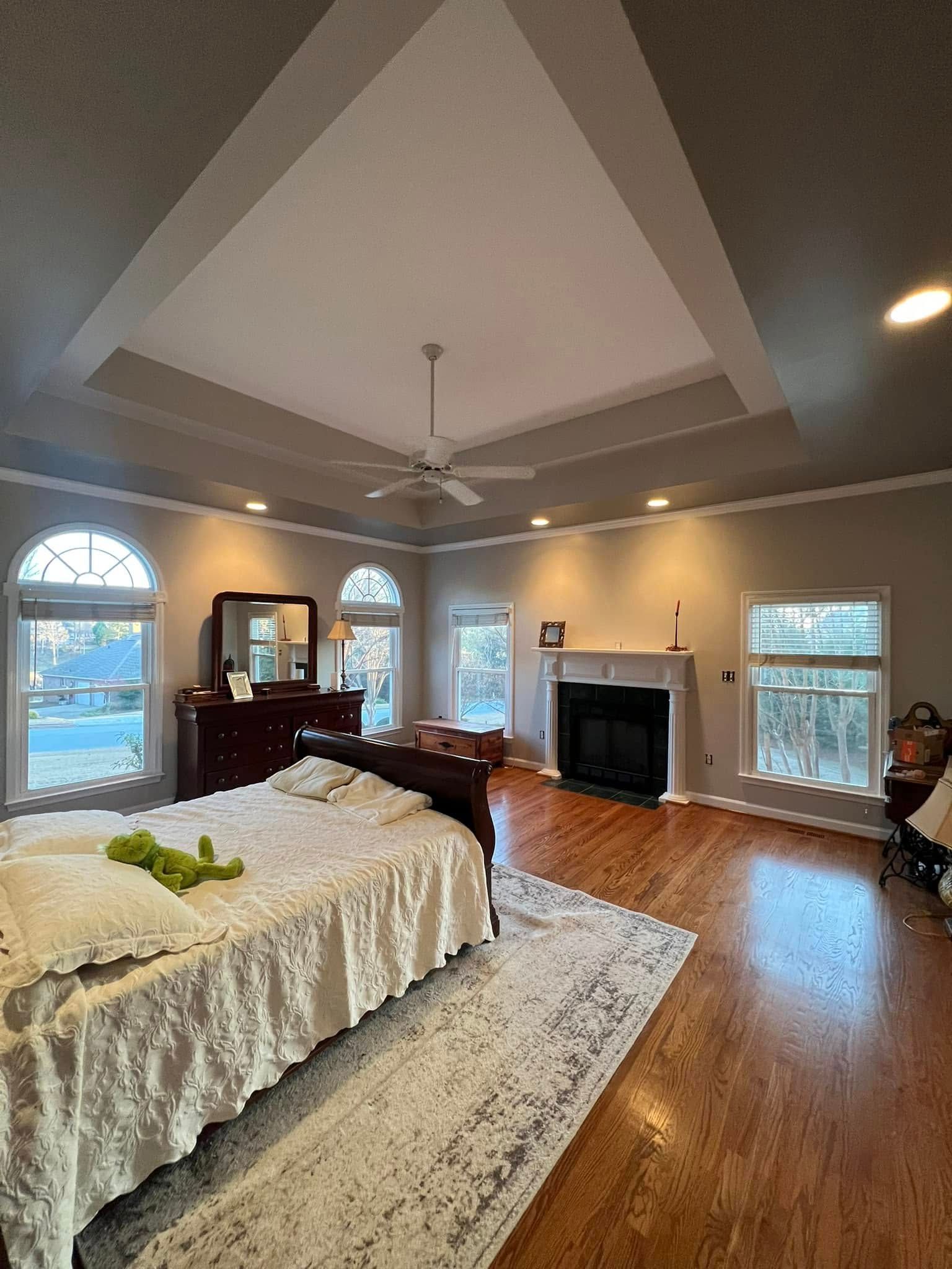 Spacious bedroom with a bed, fireplace, windows, and a tray ceiling.