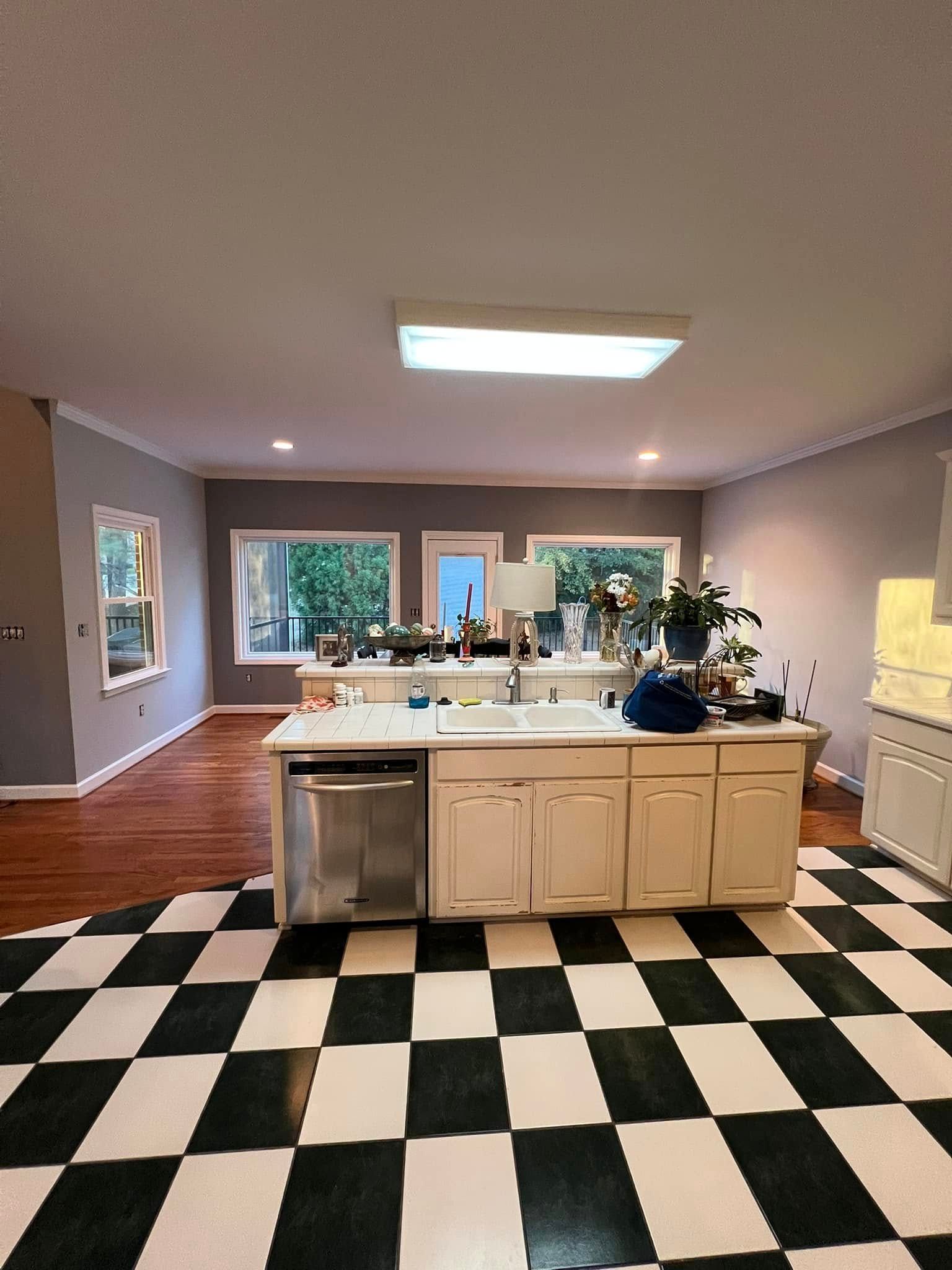 Kitchen with black and white checkered floor, white cabinets, stainless steel appliances, and gray walls.