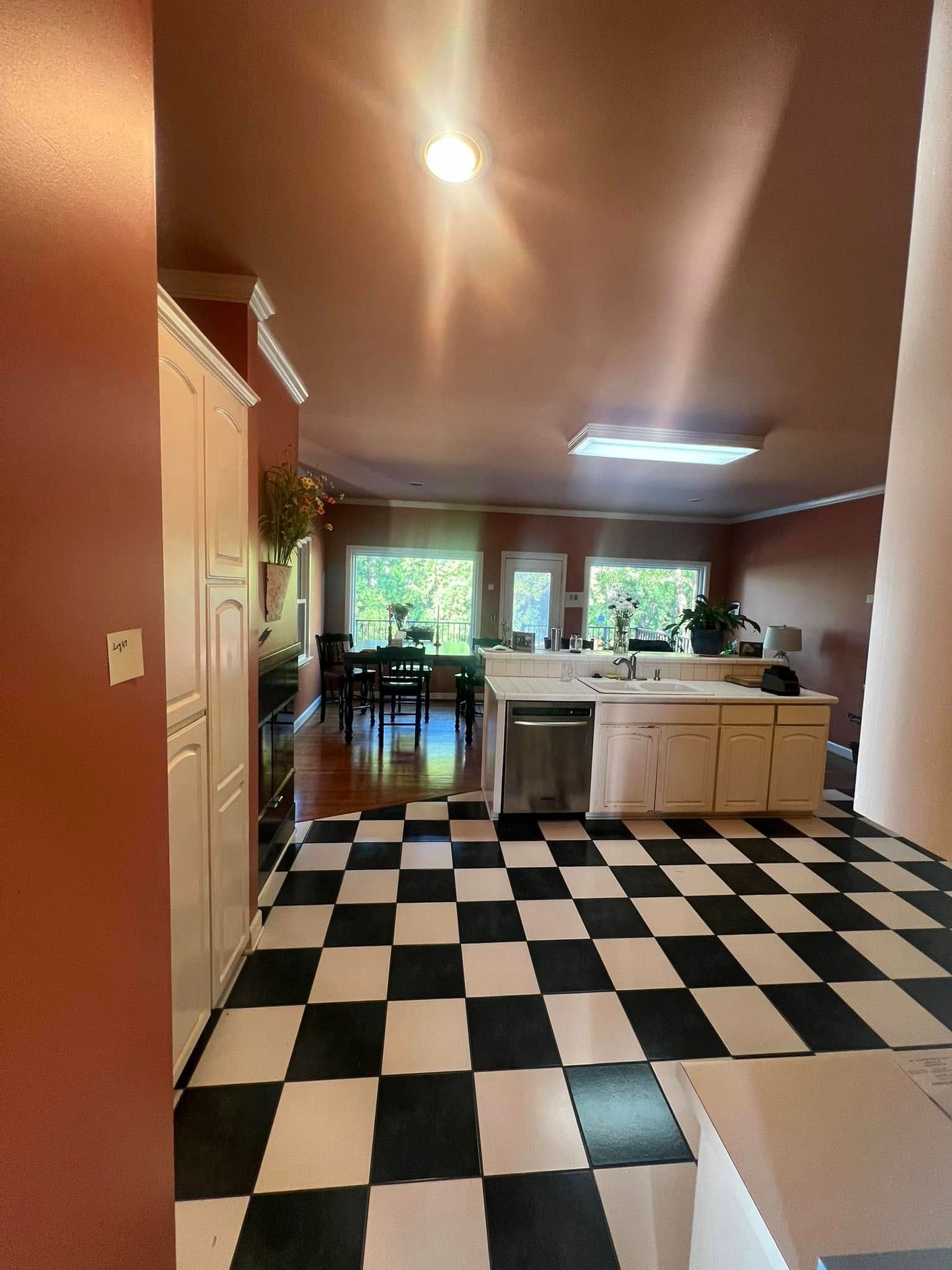 Black and white checkered floor leads to a kitchen with white cabinets, an island, and a dining area with a table.