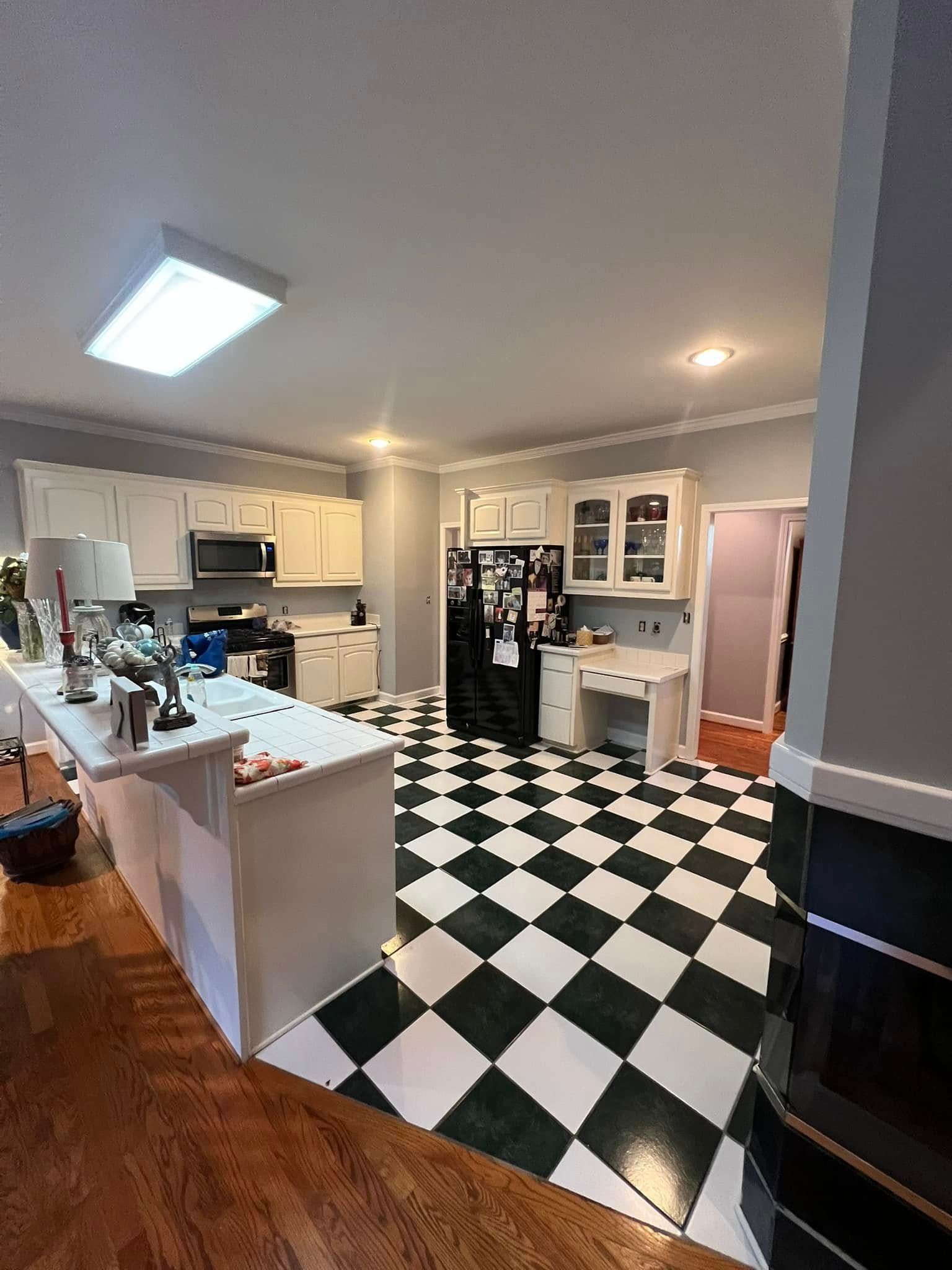 Black and white checkered floor kitchen, white cabinets, black appliances, and gray walls.