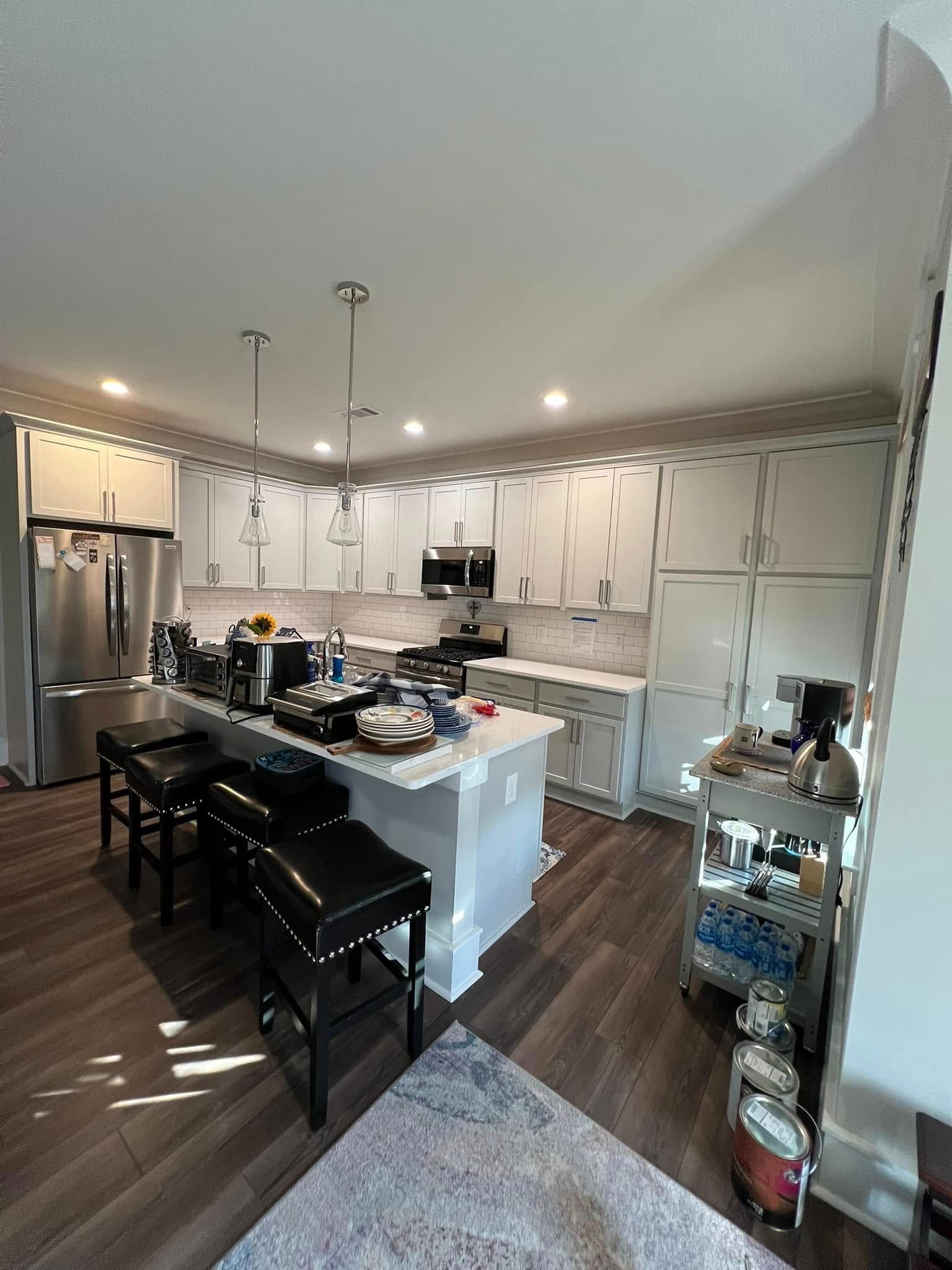 Modern kitchen with white cabinets, stainless steel appliances, island with stools, and wooden floors.
