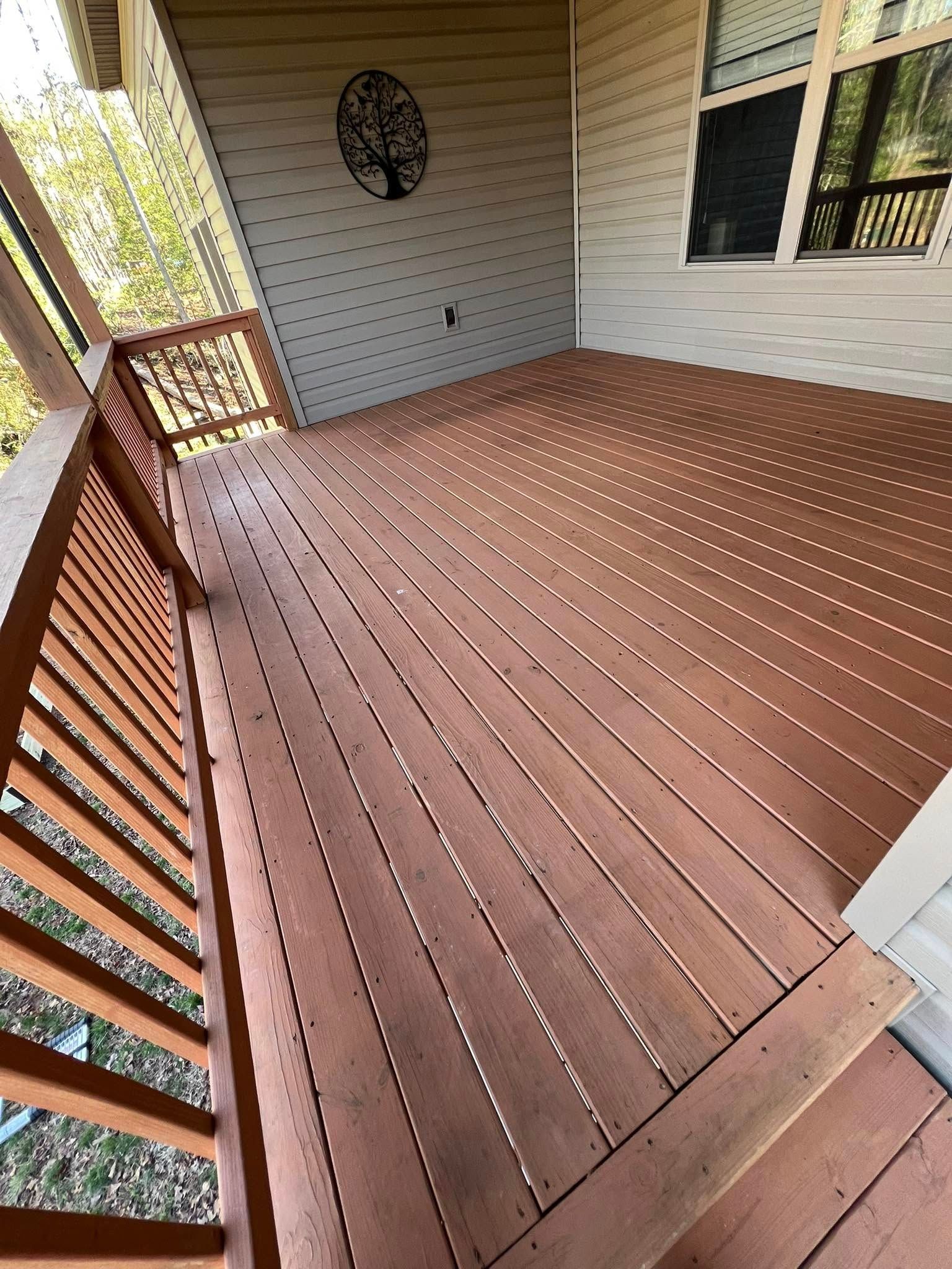 Wooden deck with railing, stained red-brown, with a decorative metal tree on the wall; bright outdoor setting.