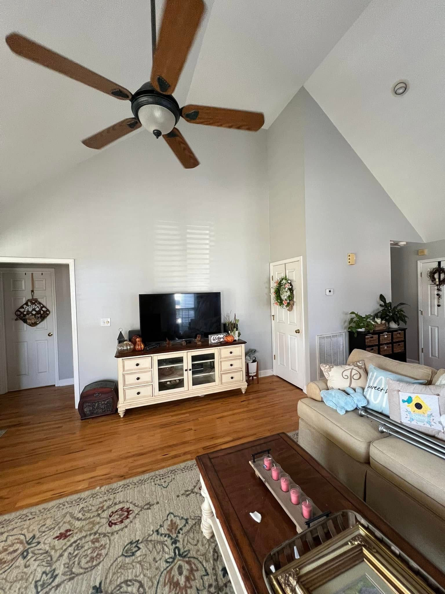 Living room with TV, beige sofa, ceiling fan, and wooden floor.