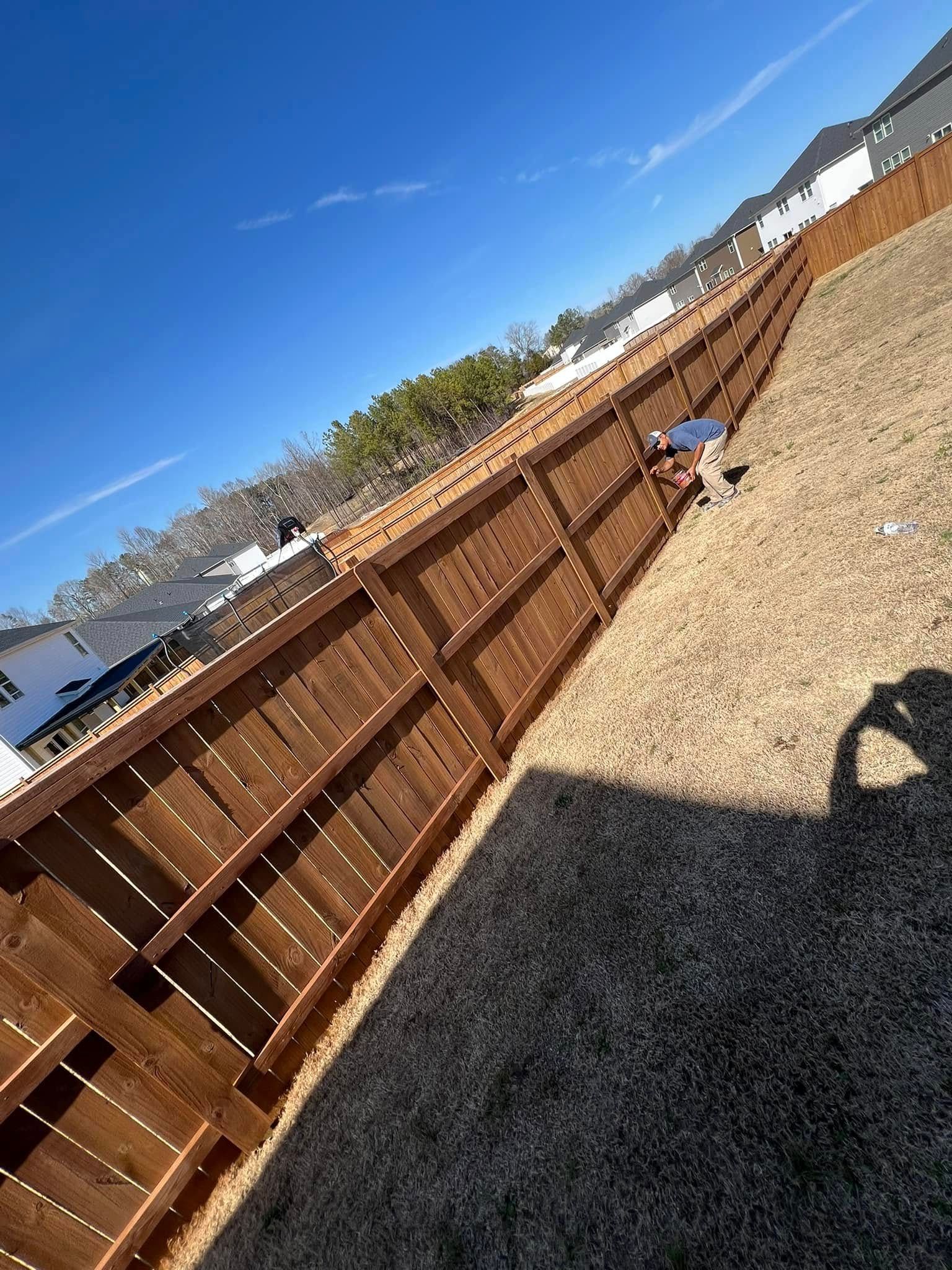 Brown wooden fence in a yard under a blue sky. Shadow of person taking photo.